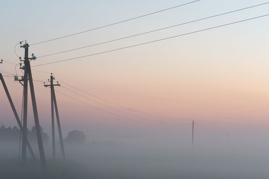 electric poles with wires in the fog in summer, beautiful nature around