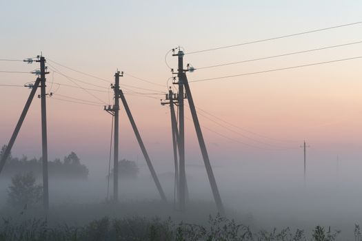 electric poles with wires in the fog in summer, beautiful nature around