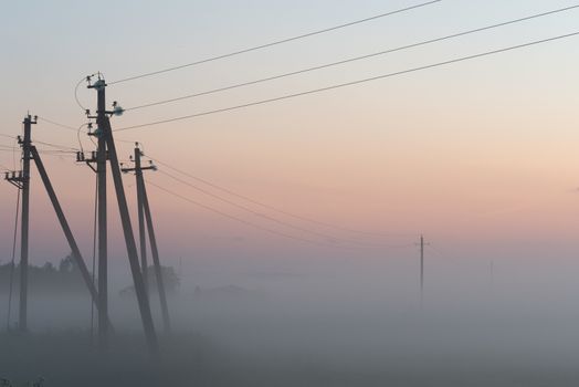 electric poles with wires in the fog in summer, beautiful nature around