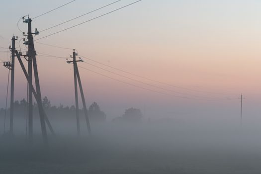 electric poles with wires in the fog in summer, beautiful nature around