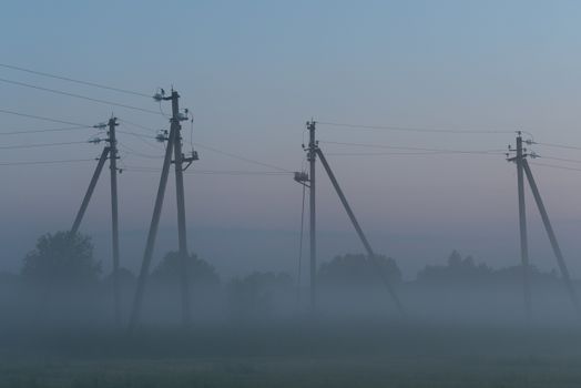 electric poles with wires in the fog in summer, beautiful nature around