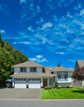 Freshly mowed lawn and main entrance of beautiful residential house on sunny day on blue sky background