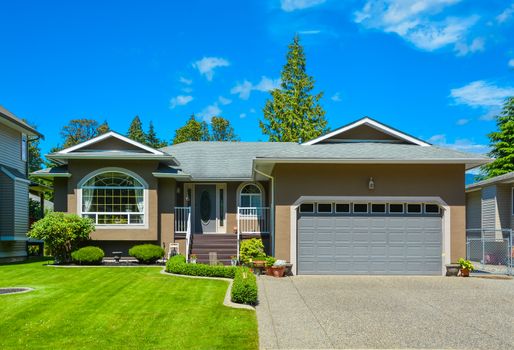 Suburban family house with nice lawn in front, wide garage door, and concrete driveway