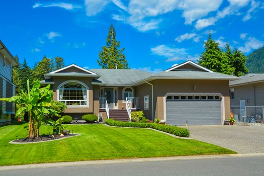 Suburban family house with nice lawn in front, wide garage door, and concrete driveway