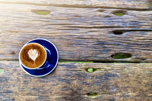 Top view of hot cappuccino coffee in the cafe, Heart shaped cream cappuccino coffee in blue cup on a wooden table with copy space.
