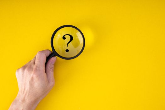 Magnifying glass with QUESTION MARK in focus on yellow background. concept of search and research.
