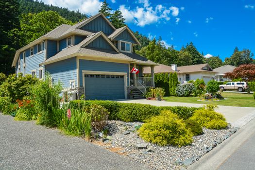 Fragment of a family house with landscaping on the front and blue sky background. House with wide garage gate