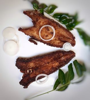 Indian restaurant style spicy fish fry place in white plate and plated beautifully with curry leaves and onions