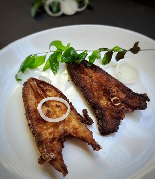 Indian restaurant style spicy fish fry place in white plate and plated beautifully with curry leaves and onions