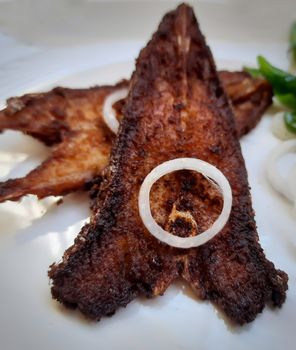 Indian restaurant style spicy fish fry place in white plate and plated beautifully with curry leaves and onions