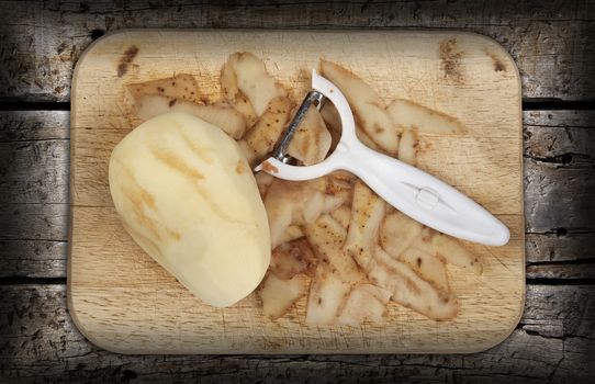 Raw potato peeled and prepared on a chopping board with a wood background and peeler