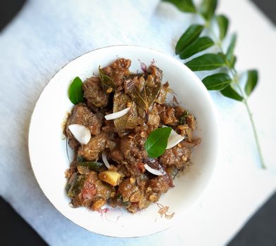 Delicious Indian style spicy pepper mutton placed beautifully in white bowl plated with onions and curry leaves and good for bones