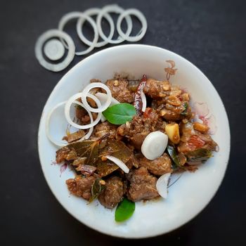 Delicious Indian style spicy pepper mutton placed beautifully in white bowl plated with onions and curry leaves and good for bones