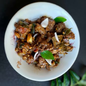 Delicious Indian style spicy pepper mutton placed beautifully in white bowl plated with onions and curry leaves and good for bones