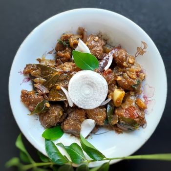 Delicious Indian style spicy pepper mutton placed beautifully in white bowl plated with onions and curry leaves and good for bones