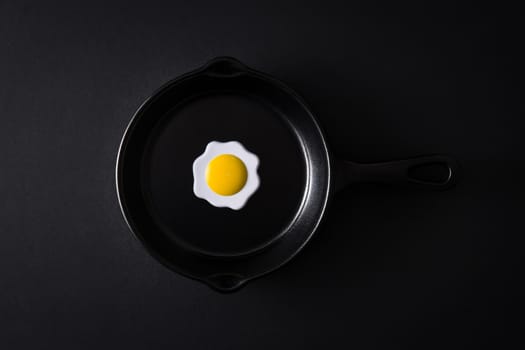 Black frying pan with egg inside on black background