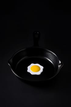 Black frying pan with egg inside on black background