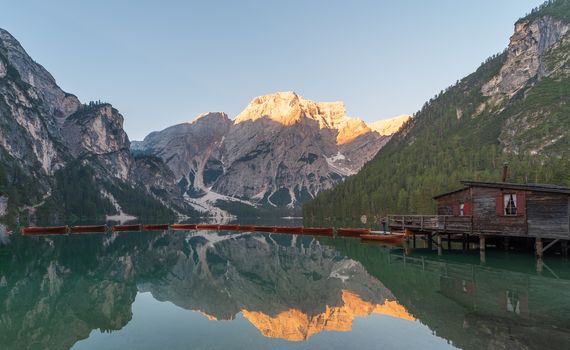 The Seekofel mountains and wooden boats reflected in the waters of Lake Braies at first light in the morning, in the Pragser Wildsee also called Lake Prags you can also see a hut, mountain landscape in the Italian Dolomites in South Tyrol