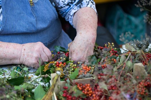 Hands of an old woman making a door wreath in autumn