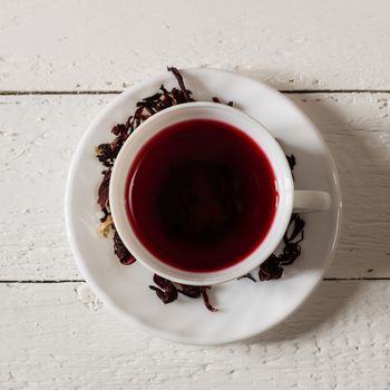 Cup of Karkadeh Red Tea with Dry Flowers on wooden table