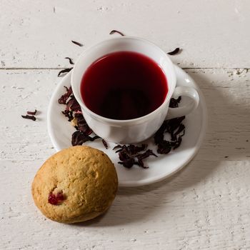 Cup of Karkadeh Red Tea with Dry Flowers and cookies on wooden table