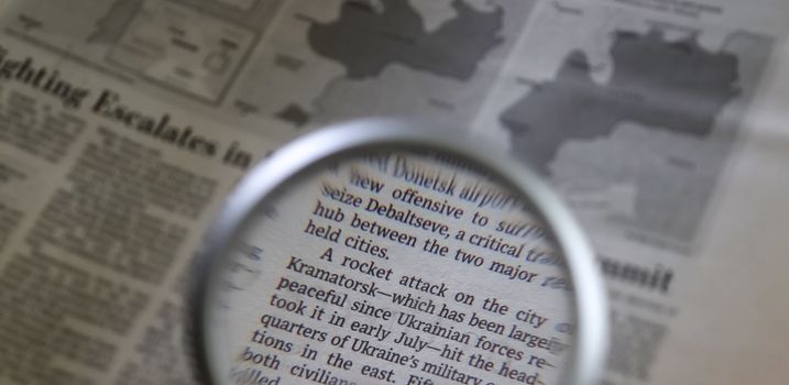 Close up view on international newspapers with a magnifying glass and a soft bokeh