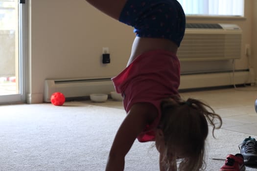 Happy little athletic girl child doing an acrobatic handstand on nature in summer park