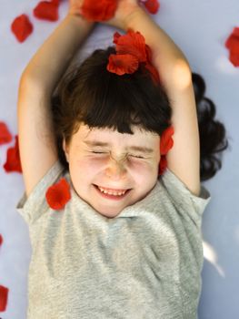 Smiling little girl squints as rose petals fall on her, vertical portrait
