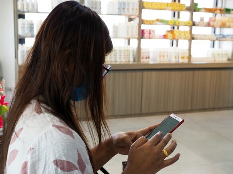 Woman sitting and using phone in the mall Along with wearing a protective face mask To help stop the spread of the COVID-19 virus. new normal concept.