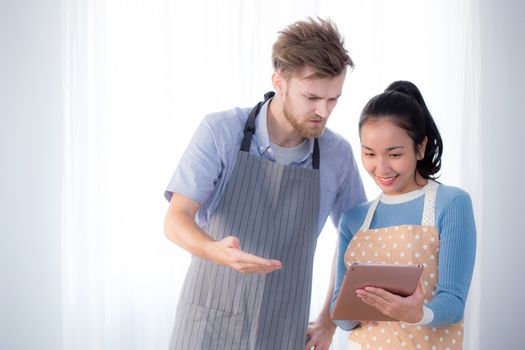 Young couple in kitchen looking at tablet - Man and girl using digital tablet in kitchen.