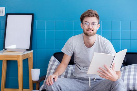Young man reading book on sofa in the living room.