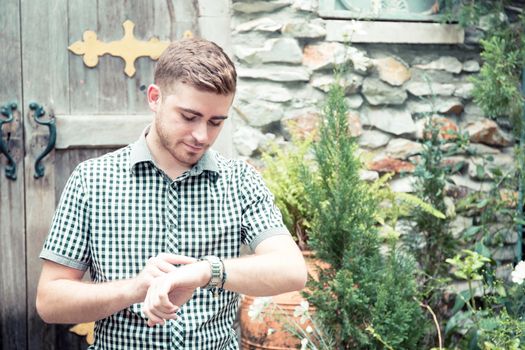 Man standing at garden looking at hand watch - Time is money.