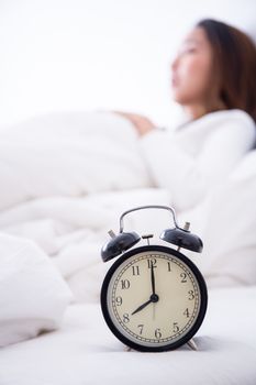 alarm clock standing on bedside table going to ring early morning to wake up woman in bed sleeping in background - early awakening -not getting enough sleep - getting work time concept