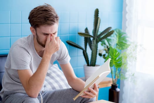 Young man reading book on sofa in the living room.