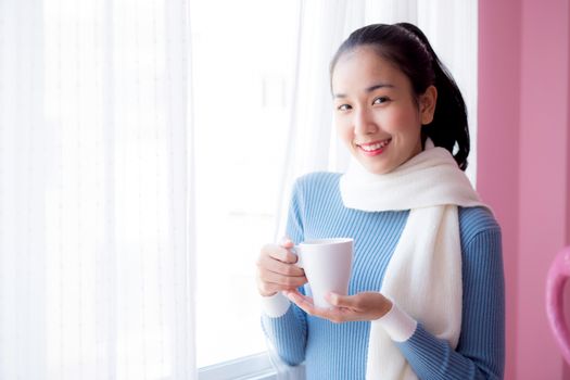 Beautiful young woman is looking out the window and holding a cup of coffee in morning.