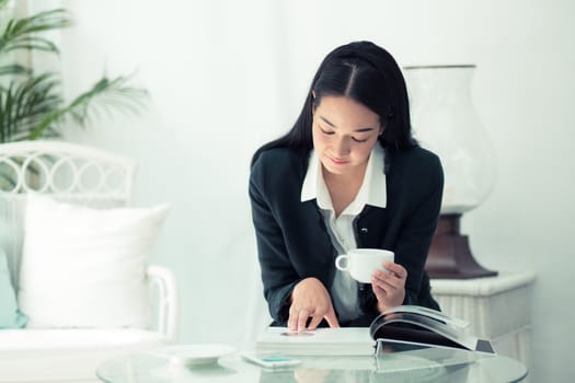 Young businesswoman sitting at table in coffee shop and reading book.