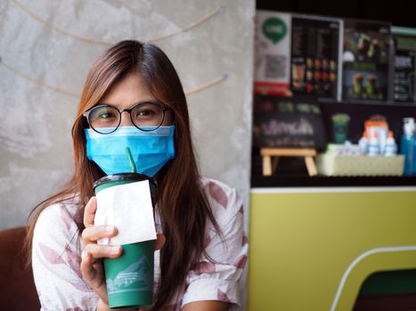 Asian woman wears a protective mask on her face while sitting in a coffee shop. New normal concept. COVID-19.