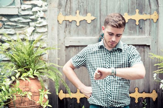 Man standing at garden looking at hand watch - Time is money.