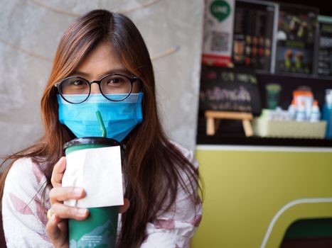 Asian woman wears a protective mask on her face while sitting in a coffee shop. New normal concept. COVID-19.