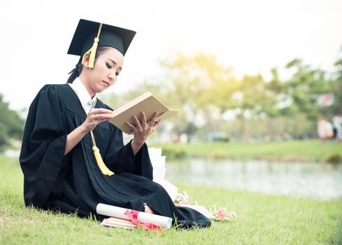 Graduate reading diary, notebook in her hand feeling relaxing and so happiness in commencement day