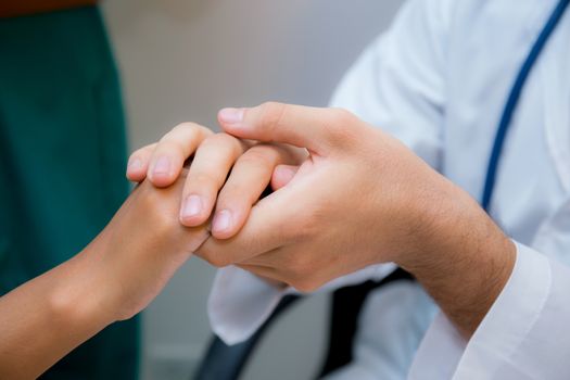 Friendly male doctor hand holding patient hand sitting at the desk for encouragement - empathy - cheering and support while medical examination.