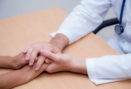 Friendly male doctor hand holding patient hand sitting at the desk for encouragement - empathy - cheering and support while medical examination.