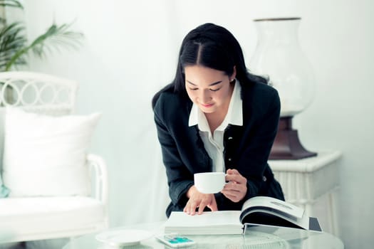 Young businesswoman sitting at table in coffee shop and reading book.