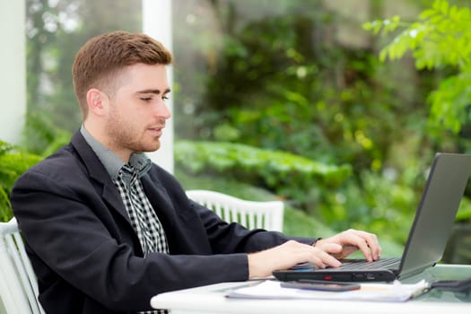 Happy young man, wearing glasses and smiling, as he work on his laptop to getearly in the living room.