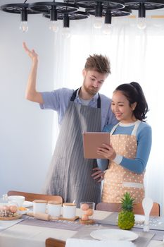 Young couple in kitchen looking at tablet - Man and girl using digital tablet in kitchen.