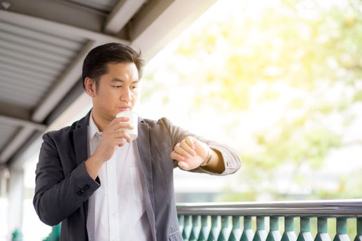 Portrait of young handsome business man drinking coffee looking at wrist watch - Waiting concept.