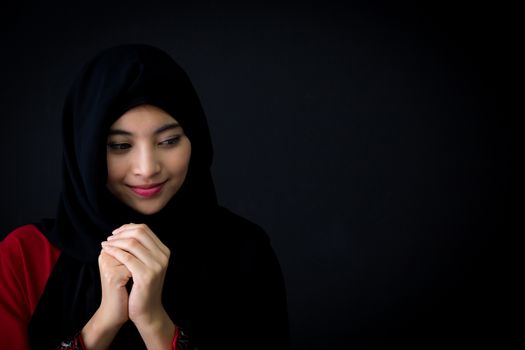religious young Muslim woman praying over black background.