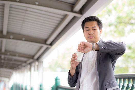 Portrait of young handsome business man drinking coffee looking at wrist watch - Waiting concept.