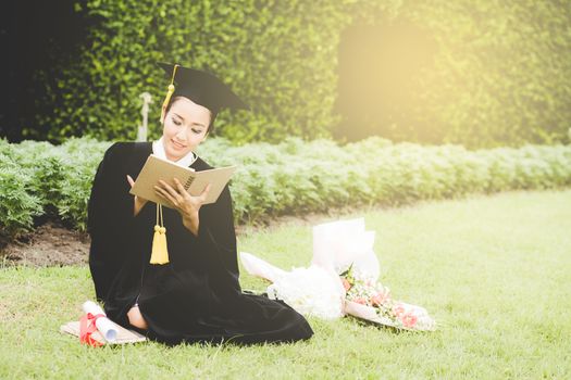 Graduate reading diary, notebook in her hand feeling relaxing and so happiness in commencement day