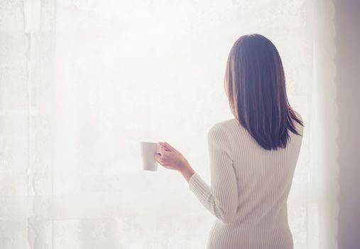 Beautiful young woman asian behind holding drinking coffee at a window.